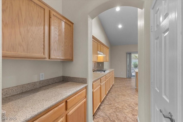 9233 Onyx Point Ct, Henderson, NV 89074 - kitchen featuring vaulted ceiling, arched walkways, light countertops, light brown cabinets, and under cabinet range hood