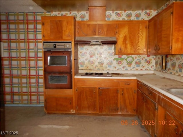 3175 Palmdale St, Las Vegas, NV 89121 - kitchen with under cabinet range hood, wallpapered walls, multiple ovens, brown cabinets, and light countertops