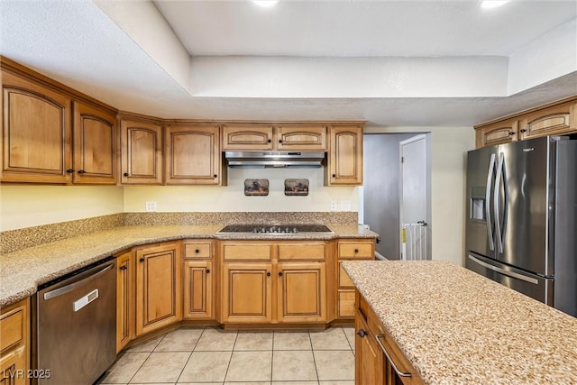 3930 Maranatha Cir, Las Vegas, NV 89103 - kitchen featuring appliances with stainless steel finishes, under cabinet range hood, brown cabinetry, light tile patterned floors, and a tray ceiling
