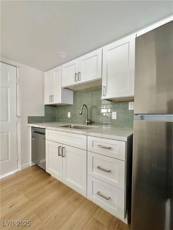 604 N Minnesota St, Las Vegas, NV 89107 - kitchen featuring appliances with stainless steel finishes, light countertops, white cabinetry, light wood-style floors, and tasteful backsplash