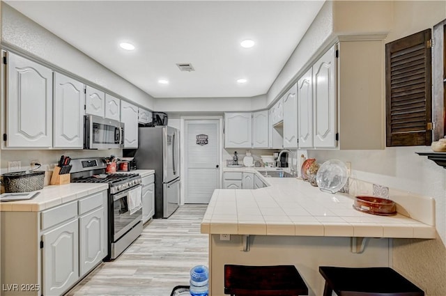 700 Capri Dr Unit 27B, Boulder City, NV 89005 - kitchen with appliances with stainless steel finishes, a peninsula, tile counters, light wood finished floors, and white cabinets