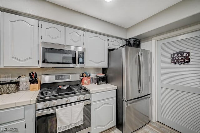 700 Capri Dr Unit 27B, Boulder City, NV 89005 - kitchen with appliances with stainless steel finishes, tile countertops, white cabinetry, and light wood-style floors