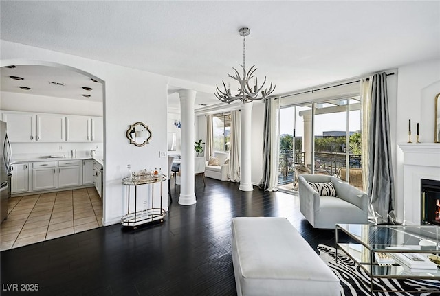 9430 Laguna Niguel Dr Unit 203, Las Vegas, NV 89134 - living room with wood finished floors, a lit fireplace, a chandelier, decorative columns, and arched walkways