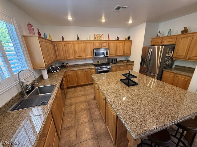 1146 Olivia Pkwy, Henderson, NV 89011 - kitchen with appliances with stainless steel finishes, a center island, a breakfast bar, tile patterned floors, and brown cabinetry