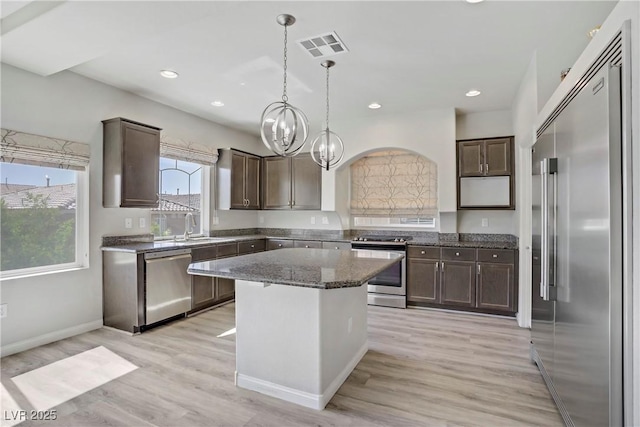 9784 Kodiak Island Ct, Las Vegas, NV 89141 - kitchen with stainless steel appliances, dark brown cabinets, dark stone countertops, a chandelier, and light wood-type flooring