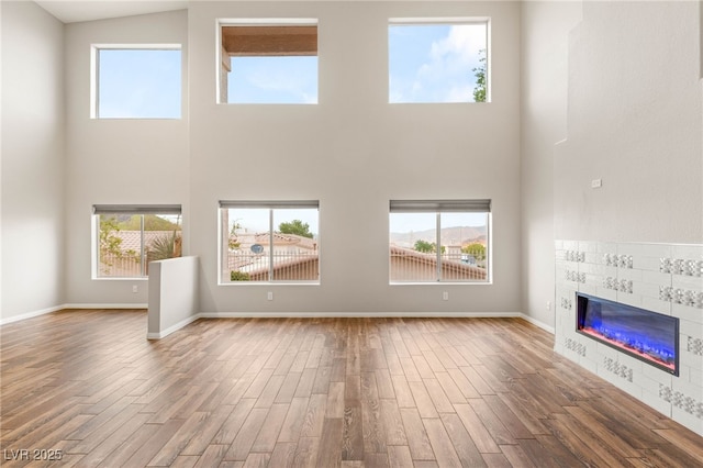 251 Big Horn Dr, Boulder City, NV 89005 - unfurnished living room with a towering ceiling, a tiled fireplace, wood finished floors, and healthy amount of natural light