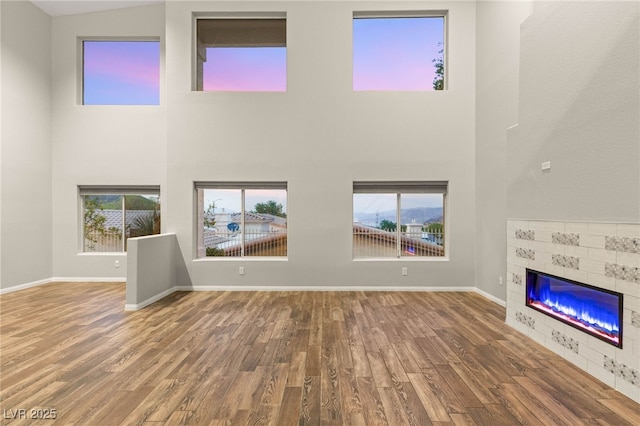 251 Big Horn Dr, Boulder City, NV 89005 - unfurnished living room featuring a tile fireplace, a towering ceiling, healthy amount of natural light, and wood finished floors
