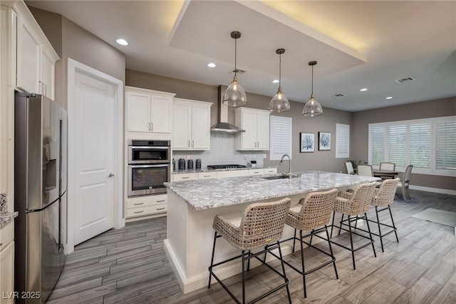 10349 Bressana Dr, Las Vegas, NV 89135 - kitchen with stainless steel appliances, wall chimney exhaust hood, light wood-style floors, recessed lighting, and a kitchen breakfast bar