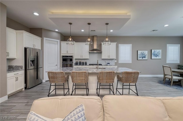 10349 Bressana Dr, Las Vegas, NV 89135 - kitchen featuring appliances with stainless steel finishes, wall chimney range hood, a kitchen breakfast bar, white cabinets, and recessed lighting