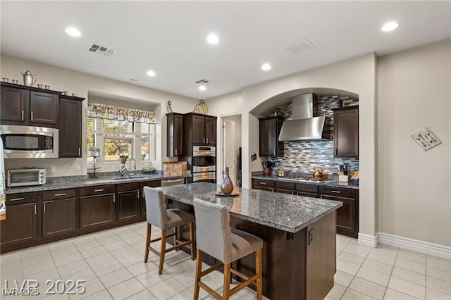 7670 Frittata Ave, Las Vegas, NV 89113 - kitchen featuring stainless steel appliances, light tile patterned floors, a kitchen island, wall chimney range hood, and a kitchen breakfast bar