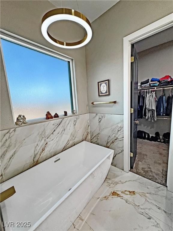2891 S Rainbow Ave, Pahrump, NV 89048 - bathroom with a soaking tub, a walk in closet, tile walls, marble tiled floors, and wainscoting