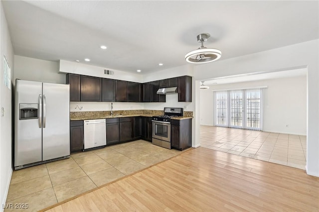 882 Westminster Ave, Las Vegas, NV 89119 - kitchen with appliances with stainless steel finishes, under cabinet range hood, light stone counters, light tile patterned floors, and dark brown cabinetry