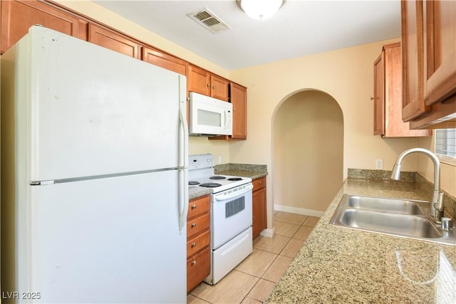 1836 N Decatur Blvd Unit 203, Las Vegas, NV 89108 - kitchen featuring white appliances, brown cabinetry, light tile patterned flooring, arched walkways, and light countertops