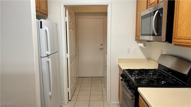 7163 S Durango Dr Unit 113, Las Vegas, NV 89113 - kitchen featuring gas stove, stainless steel microwave, freestanding refrigerator, brown cabinetry, and light tile patterned flooring