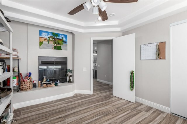 7135 Polaris Ave, Las Vegas, NV 89118 - living room with a tray ceiling, wood finished floors, ceiling fan, and a glass covered fireplace