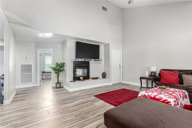 7135 Polaris Ave, Las Vegas, NV 89118 - living room featuring wood finished floors, a towering ceiling, ceiling fan, and a glass covered fireplace