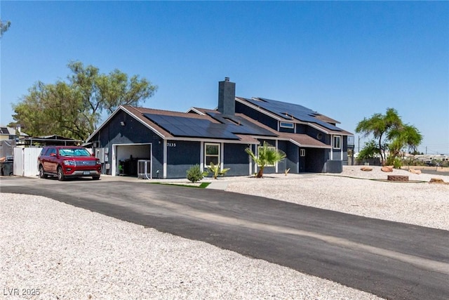 7135 Polaris Ave, Las Vegas, NV 89118 - view of front of house with an attached garage, solar panels, a chimney, and asphalt driveway