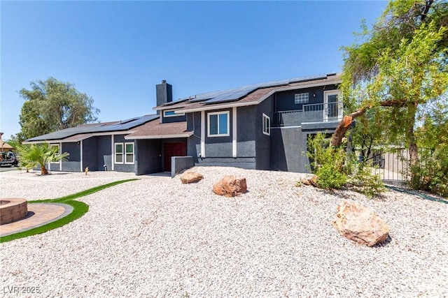 7135 Polaris Ave, Las Vegas, NV 89118 - view of front of house featuring a fire pit, roof mounted solar panels, a chimney, a balcony, and stucco siding