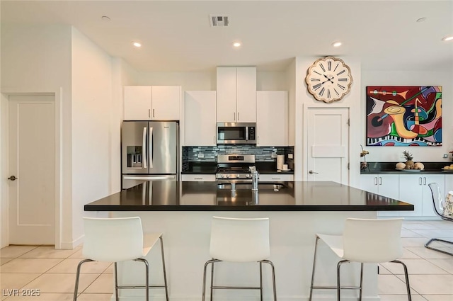 3194 Lumassina Way, Henderson, NV 89044 - kitchen with stainless steel appliances, a kitchen bar, dark countertops, light tile patterned floors, and decorative backsplash