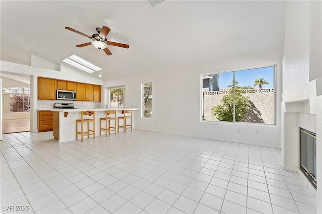 1908 Summit Pointe Dr, Las Vegas, NV 89117 - unfurnished living room with ceiling fan, lofted ceiling, a glass covered fireplace, a skylight, and light tile patterned floors