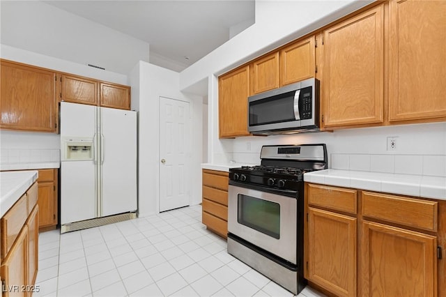 1908 Summit Pointe Dr, Las Vegas, NV 89117 - kitchen with stainless steel appliances, light tile patterned flooring, tile countertops, and brown cabinetry