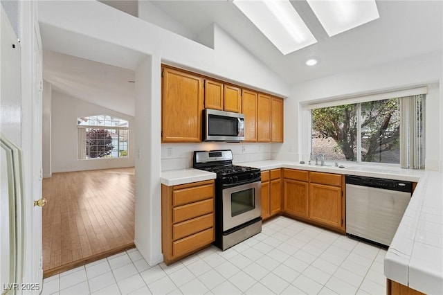 1908 Summit Pointe Dr, Las Vegas, NV 89117 - kitchen featuring stainless steel appliances, lofted ceiling, tile counters, healthy amount of natural light, and brown cabinetry