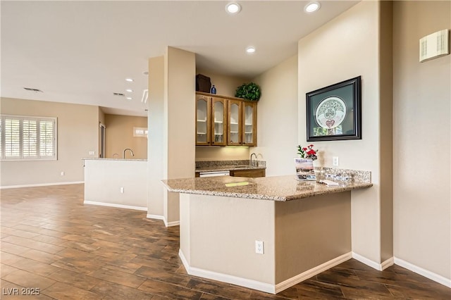 1637 Wellington Springs Ave, Henderson, NV 89052 - kitchen featuring glass insert cabinets, dark wood-style flooring, recessed lighting, light stone countertops, and a peninsula