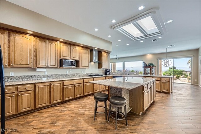 1637 Wellington Springs Ave, Henderson, NV 89052 - kitchen featuring appliances with stainless steel finishes, wall chimney range hood, a kitchen bar, wood finished floors, and recessed lighting