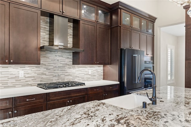 10179 Emerald Sunset Ct, Las Vegas, NV 89148 - kitchen with wall chimney range hood, appliances with stainless steel finishes, decorative backsplash, glass insert cabinets, and dark brown cabinets