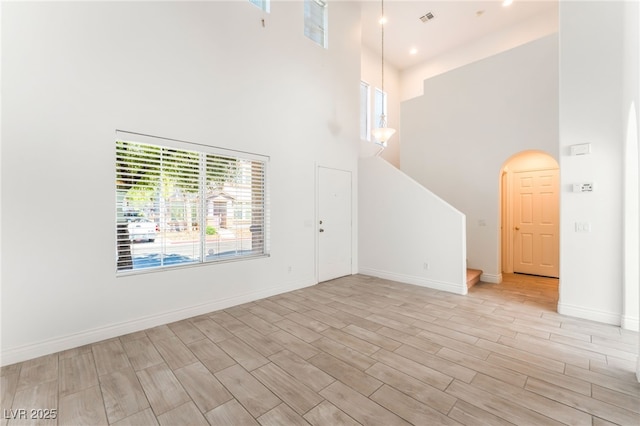 5340 Santa Fe Heights St, North Las Vegas, NV 89081 - unfurnished living room featuring a towering ceiling, stairway, arched walkways, and light wood-style flooring