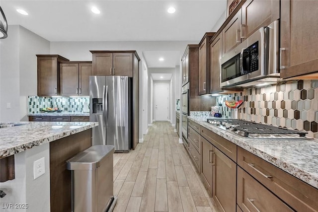 5801 Exbury Gardens Ct, Las Vegas, NV 89118 - kitchen featuring appliances with stainless steel finishes, light stone countertops, backsplash, light wood-style floors, and recessed lighting