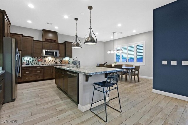 5801 Exbury Gardens Ct, Las Vegas, NV 89118 - kitchen with appliances with stainless steel finishes, light wood finished floors, tasteful backsplash, dark brown cabinets, and a breakfast bar