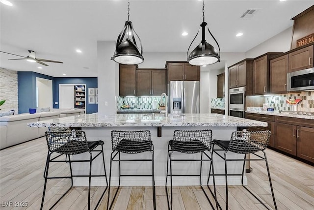 5801 Exbury Gardens Ct, Las Vegas, NV 89118 - kitchen featuring appliances with stainless steel finishes, open floor plan, ceiling fan, backsplash, and light stone counters