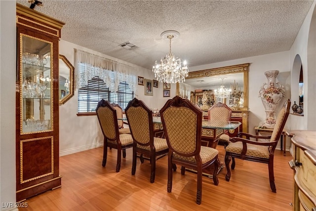 3877 Platis Cir, Las Vegas, NV 89103 - dining space featuring a chandelier, light wood-style flooring, a textured ceiling, and arched walkways
