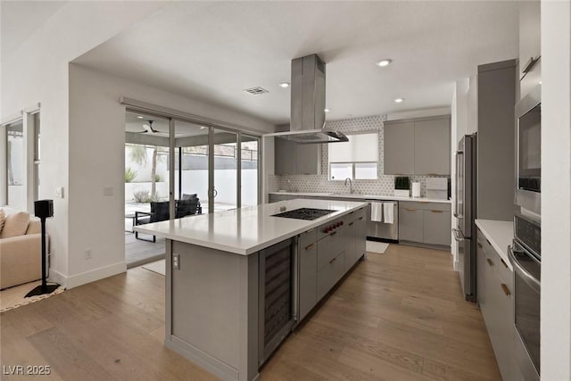 9789 Twilight Moon Ave, Las Vegas, NV 89148 - kitchen featuring gray cabinets, wine cooler, stainless steel appliances, tasteful backsplash, and island range hood