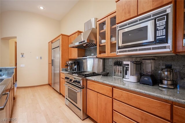 15 Emerald Dunes Cir, Henderson, NV 89052 - kitchen featuring premium appliances, wall chimney exhaust hood, light wood-style flooring, decorative backsplash, and lofted ceiling