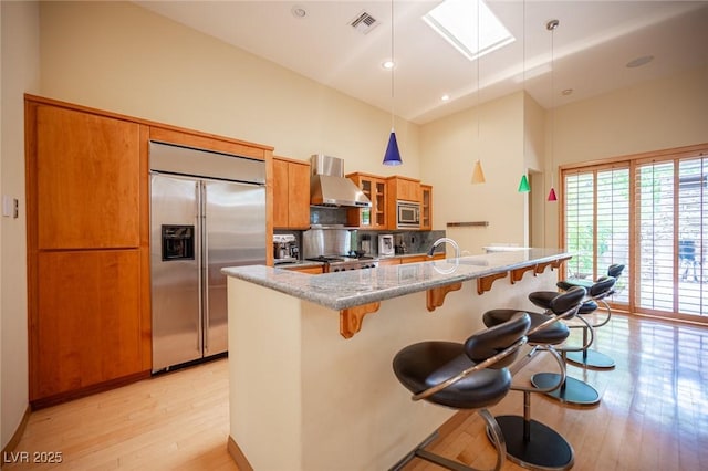 15 Emerald Dunes Cir, Henderson, NV 89052 - kitchen with built in appliances, wall chimney range hood, high vaulted ceiling, brown cabinets, and light wood-style floors