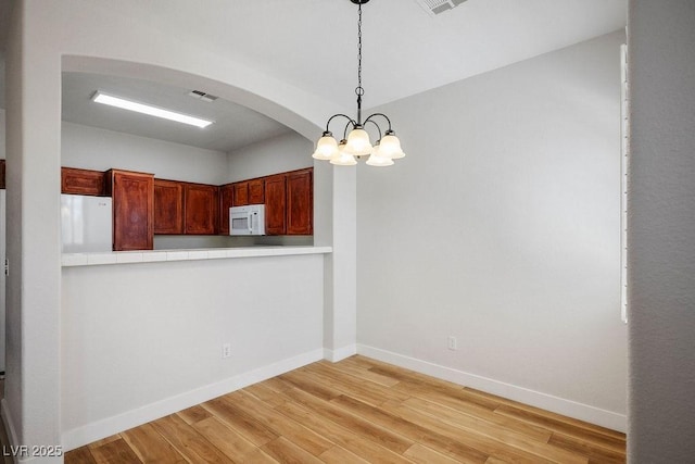 901 Nevada Sky St, Las Vegas, NV 89128 - kitchen featuring white microwave, arched walkways, refrigerator, hanging light fixtures, and light wood-style flooring