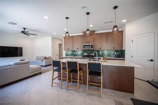 9451 Lunar Ray St, Las Vegas, NV 89143 - kitchen with stainless steel appliances, light countertops, tasteful backsplash, light tile patterned floors, and a center island with sink