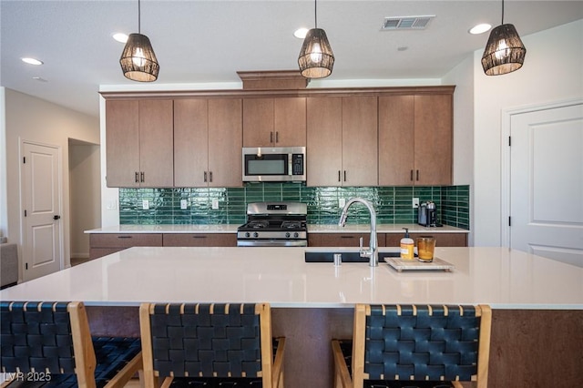 9451 Lunar Ray St, Las Vegas, NV 89143 - kitchen with appliances with stainless steel finishes, light countertops, decorative backsplash, hanging light fixtures, and a center island with sink