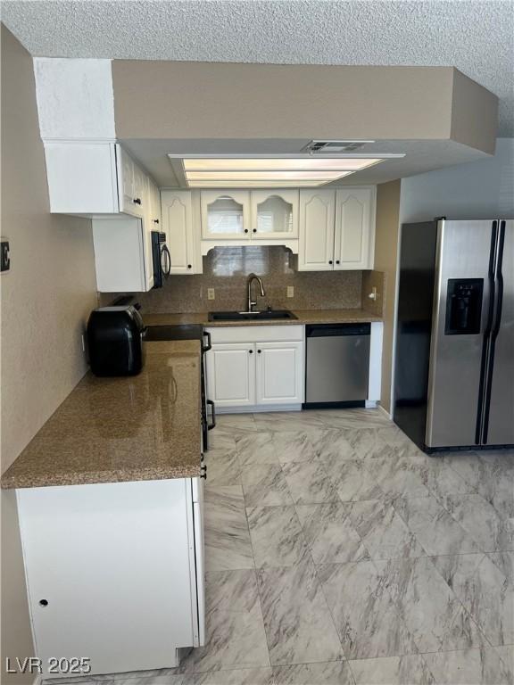 901 Sulphur Springs Ln Unit 101, Las Vegas, NV 89128 - kitchen featuring appliances with stainless steel finishes, tasteful backsplash, white cabinetry, glass insert cabinets, and a textured ceiling