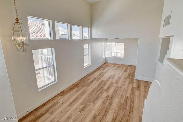 1716 Klamath Falls Way, Las Vegas, NV 89128 - unfurnished living room with a towering ceiling, a chandelier, and light wood-style flooring