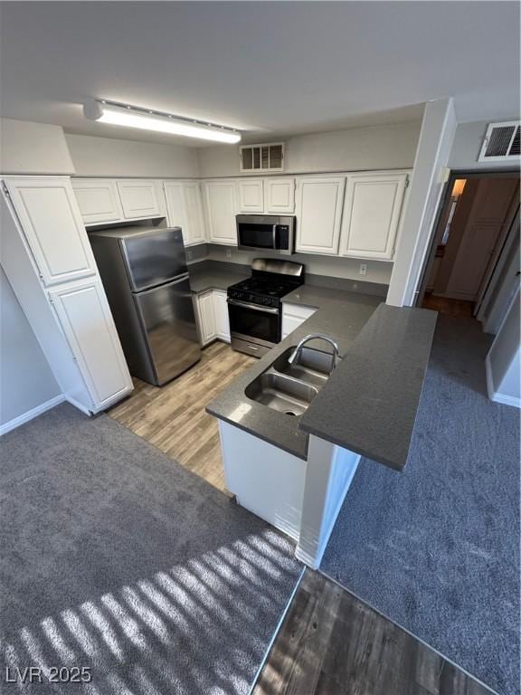5710 E Tropicana Ave Unit 2225, Las Vegas, NV 89122 - kitchen with appliances with stainless steel finishes, dark countertops, a peninsula, white cabinetry, and light wood-style floors