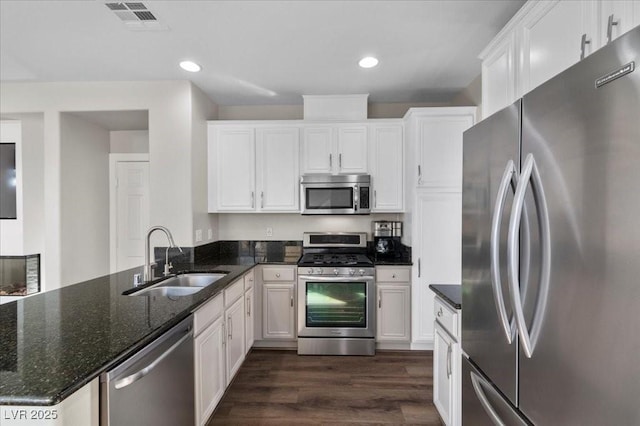 8353 Lower Trailhead Ave, Las Vegas, NV 89113 - kitchen with appliances with stainless steel finishes, a peninsula, white cabinets, dark wood finished floors, and dark stone countertops