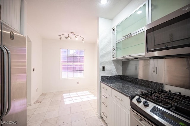 10414 Midseason Mist St, Las Vegas, NV 89183 - kitchen with appliances with stainless steel finishes, white cabinets, dark stone counters, glass insert cabinets, and light tile patterned floors