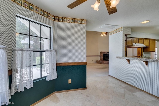 5505 Excelsior Springs Ln, Las Vegas, NV 89130 - kitchen with a ceiling fan, brown cabinetry, light stone counters, a brick fireplace, and under cabinet range hood