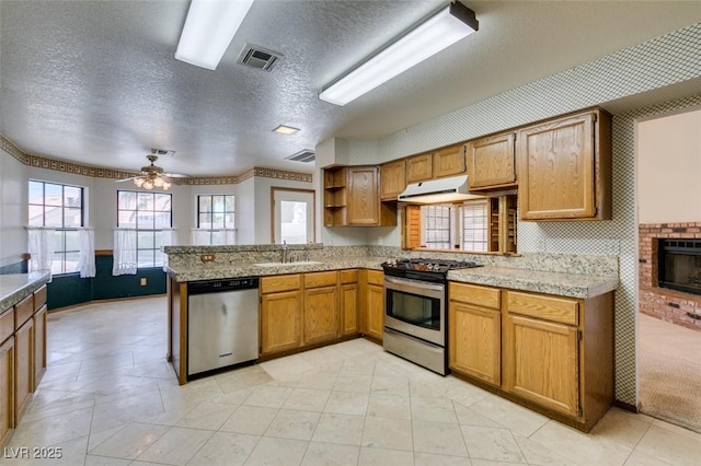 5505 Excelsior Springs Ln, Las Vegas, NV 89130 - kitchen with stainless steel appliances, under cabinet range hood, a peninsula, brown cabinets, and a textured ceiling