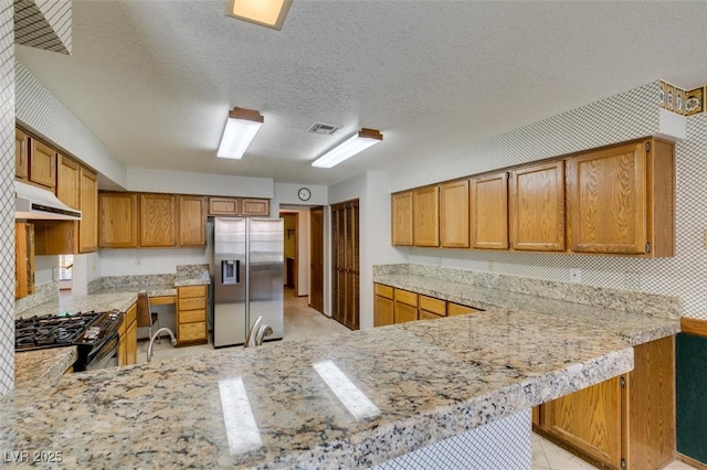 5505 Excelsior Springs Ln, Las Vegas, NV 89130 - kitchen with stainless steel fridge, black range with gas cooktop, under cabinet range hood, a peninsula, and brown cabinets