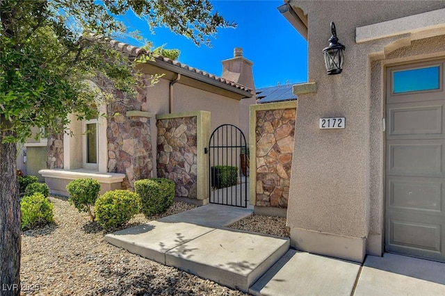 2172 De Rouge Ave, Henderson, NV 89044 - view of exterior entry featuring stone siding, a gate, a chimney, stucco siding, and solar panels