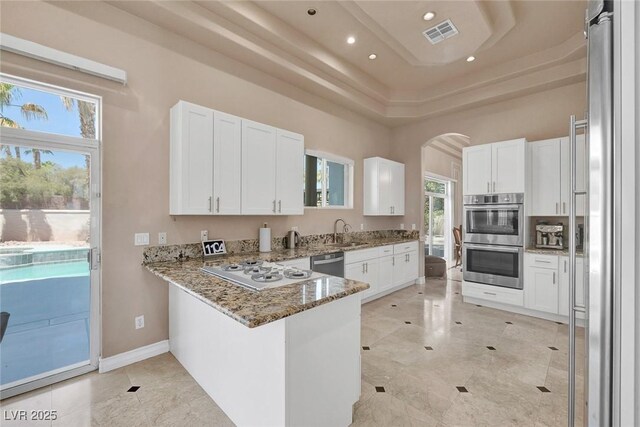 2209 Purple Majesty Ct, Las Vegas, NV 89117 - kitchen with stainless steel appliances, a raised ceiling, light stone counters, arched walkways, and recessed lighting